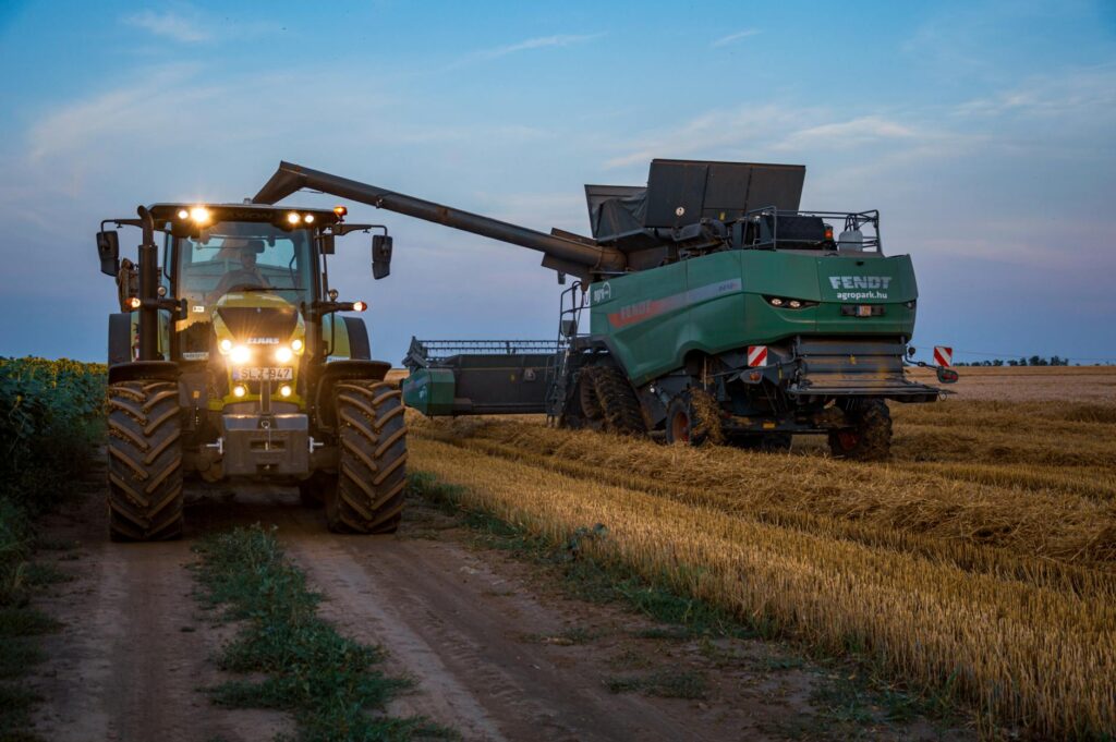 Tractor and harvester working in a field at dusk, showcasing rural agriculture machinery.